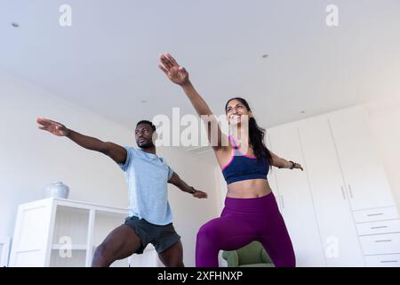 Practicing yoga, man and woman doing warrior pose in living room Stock Photo