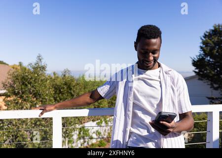 Smiling man using smartphone while standing on balcony, enjoying outdoor view Stock Photo