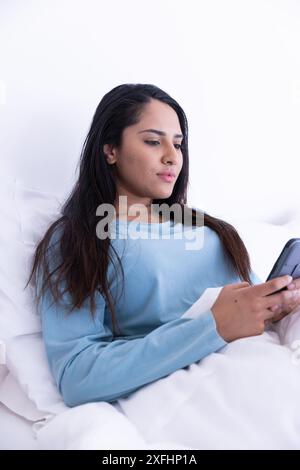 Relaxing in bed, woman using smartphone while resting in comfortable setting Stock Photo