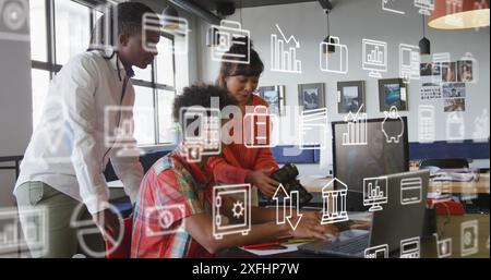 Image of multiple icons over diverse coworkers discussing reports on desktop in office Stock Photo