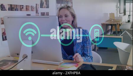 Image of flowchart of icons over caucasian woman picking up cellphone while working on desktop Stock Photo