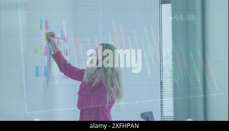 Image of graphs, numbers, caucasian woman talking on cellphone and writing on sticky notes Stock Photo