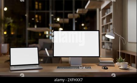 A modern home office workspace or private office at night features a laptop and computer with white-screens mockup on a wooden table. 3d render, 3d il Stock Photo