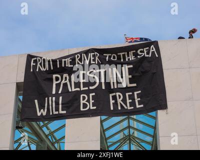 04 July 2024, Australia, Canberra, Parliament House. Pro-Palestine protester scale the roof of Australia's Parliament House to unfurl banners criticising the Australian's government's role in facilitating the genocide in Gaza Stock Photo