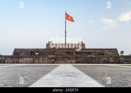 Wonderful view of a square and the flag of Vietnam (red flag with a gold star) fluttering over a tower of the Citadel on blue sky background in Hue. Stock Photo