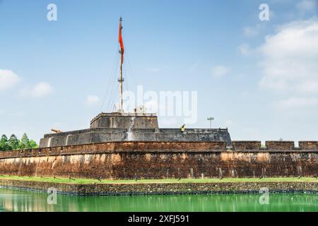 Wonderful view of a square and the flag of Vietnam (red flag with a gold star) fluttering over a tower of the Citadel on blue sky background in Hue. Stock Photo