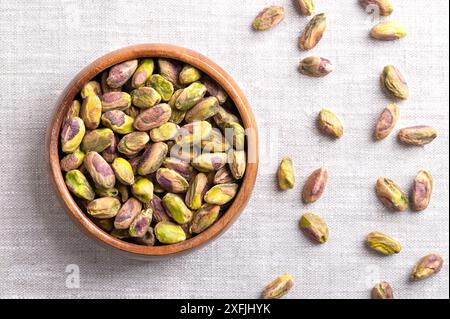 Pistachios kernels, roasted and salted nuts in a wooden bowl on linen fabric. Shelled and crunchy toasted fruits of Pistacia vera. Ready-to-eat snack. Stock Photo