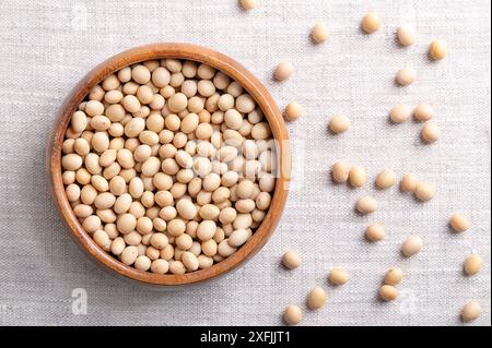 Dried soybeans, also soy beans or soya beans in a wooden bowl on linen fabric. Whole and raw seeds of the legume and oilseed Glycine max. Stock Photo
