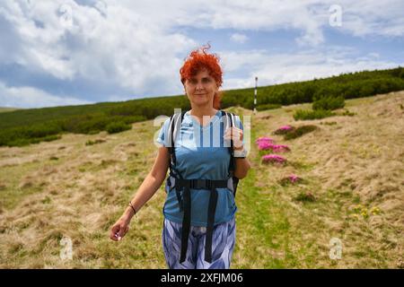 Woman hiker with backpack hiking on a mountain among pink rhododendron flowers in bloom Stock Photo