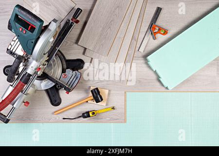 laying new laminate or vinyl flooring. Tools like chop saw hammer rolling measure gray laminate tiles on footstep sound insulation. diy professional h Stock Photo