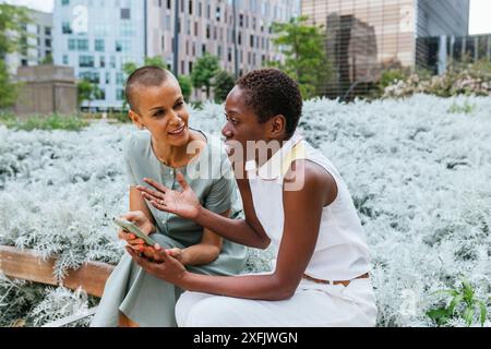 Two professional women engaged in a serious conversation with smartphone in an urban garden Stock Photo