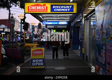 Signage outside Chemist Warehouse, with one glowing bright sign above the store entrance and another sign on the footpath, as people walk by Stock Photo