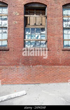 Abandoned brick industrial building with broken and weather worn windows next to parking spot Stock Photo