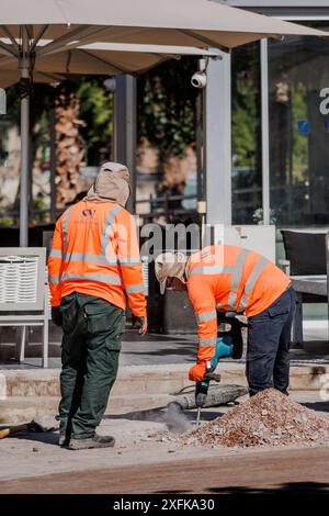 Two road workers in reflector vests using jackhammer, drilling, breaking asphalt. Discussing. Road repair Stock Photo