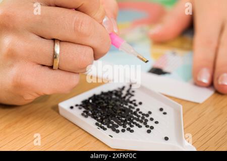 A close-up of a hand placing crystals on a canvas for a diamond painting project. Diamond Mosaic Stock Photo