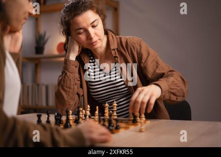 Two women playing chess at home, focused on the game, enjoying leisure time Stock Photo