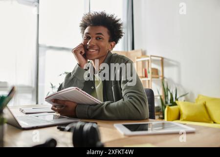 A young black man is focused on his laptop and notebook while studying at his home desk. Stock Photo