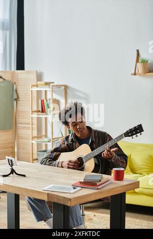 A man of African American descent sits at a table, engrossed in playing an acoustic guitar. Stock Photo