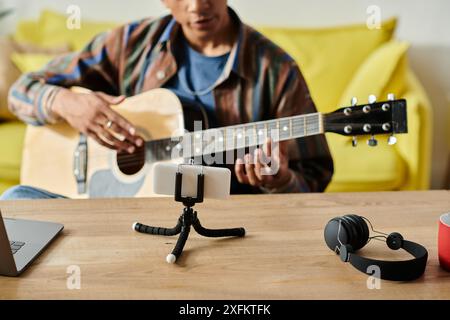 A young African American musician plays an acoustic guitar on a table while filming for his blog. Stock Photo