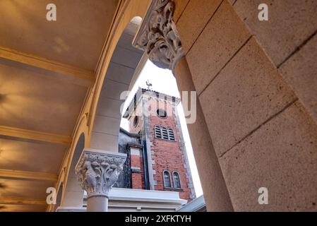 View of bell tower of an abbey through an arch formed by Corinthian columns. At the top of the tower, there is a black rooster weather vane, contrasti Stock Photo