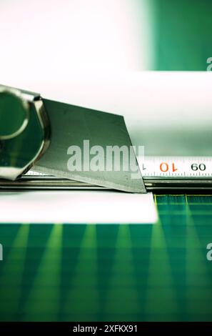 A sharp utility knife is being used to cut a piece of white paper on a green cutting mat Stock Photo