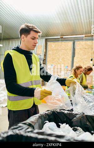 A young man in a yellow safety vest diligently picks up trash with other eco-conscious volunteers in gloves. Stock Photo