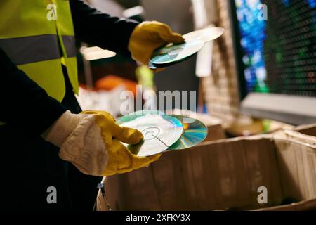 A young volunteer in a yellow safety vest sorts waste, holding cd with eco-conscious intentions. Stock Photo