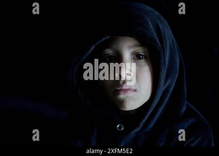 Close-up portrait of little boy on black hoodie looking at the camera with a sad expression on his face. Copy space and balck background Stock Photo