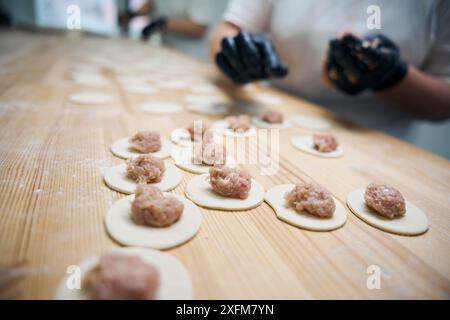Kitchen worker lays out pieces of minced meat on blanks for dumplings Stock Photo