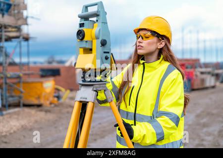 Female site engineer surveyor working with theodolite total station EDM equipment on a building construction site outdoors Stock Photo