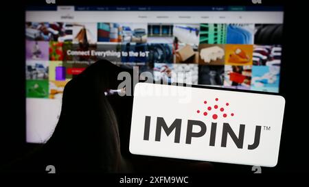 Person holding smartphone with logo of US RFID company Impinj Inc. in front of website. Focus on phone display. Stock Photo