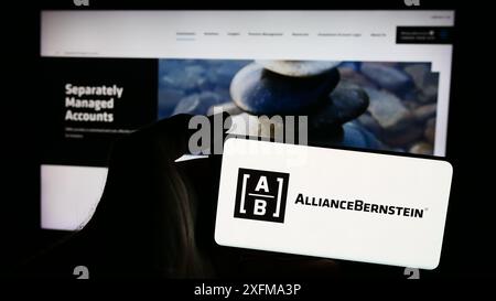 Person holding mobile phone with logo of US investment company AllianceBernstein Holding LP (AB) in front of web page. Focus on phone display. Stock Photo