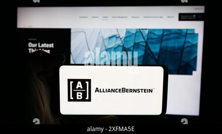 Person holding cellphone with logo of US investment company AllianceBernstein Holding L.P. (AB) in front of webpage. Focus on phone display. Stock Photo