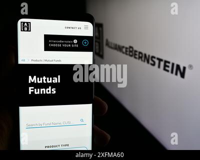 Person holding cellphone with webpage of US investment company AllianceBernstein Holding L.P. (AB) with logo. Focus on center of phone display. Stock Photo