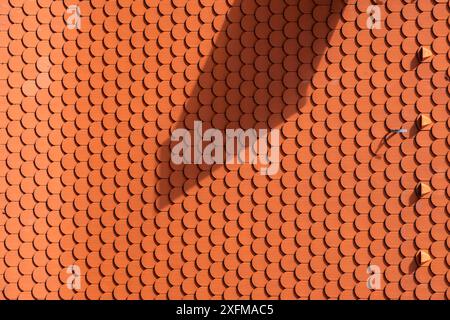 A red roof with a shadow of a knife on it. The shadow is dark and elongated, creating a sense of depth and dimension in the scene Stock Photo