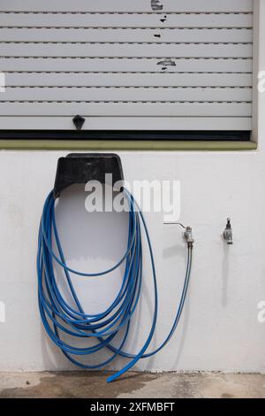 A blue hose is attached to a wall. The hose is connected to a faucet Stock Photo