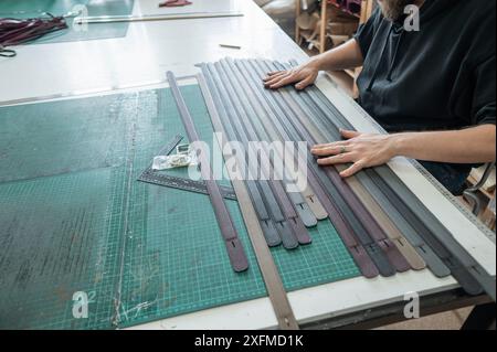 A tanner makes leather belts in a workshop. Close-up of a man's hands. Stock Photo