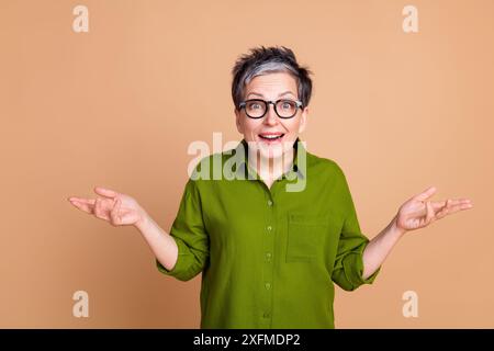 Photo portrait of attractive retired woman amazed raise hands dressed stylish green clothes isolated on beige color background Stock Photo