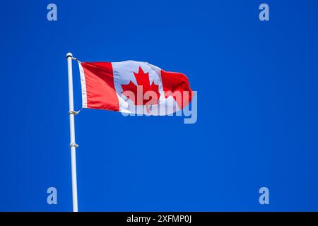 A red and white Canadian flag against a clear blue sky background Stock Photo