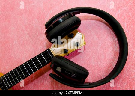 Close-up of a guitar headstock with black headphones on a pink background, depicting music and creativity. Stock Photo