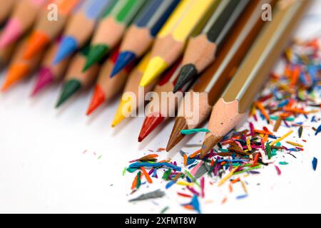 Close-up of vibrant colored pencils arranged neatly with pencil shavings scattered on a white surface, emphasizing creativity and art. Stock Photo