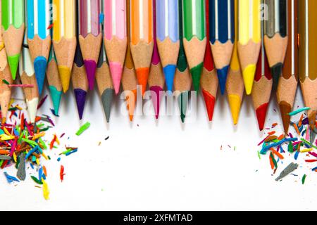 A row of sharpened colored pencils lies on a white surface, with shavings scattered on either side. The pencils are arranged in a line, with their poi Stock Photo