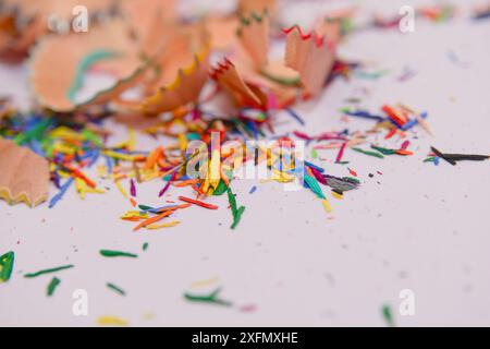 A close-up image of colorful pencil shavings scattered on a white surface. The shavings are from a variety of colored pencils and are arranged in a ra Stock Photo