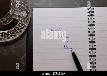 A pen is on a notebook with the words World Poetry Day written on it. A cup of tea is on the table next to the notebook Stock Photo
