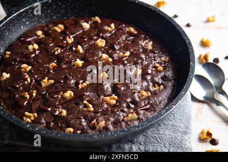 Homemade brownie cooked in a skillet, not baked, with nuts, chocolate chips on a white table Stock Photo