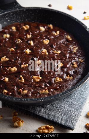 Homemade brownie cooked in a skillet, not baked, with nuts, melted chocolate and chocolate chips on a white table Stock Photo