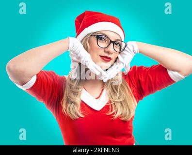 Young blonde haired woman dressed as Santa Claus with glasses looking at camera isolated on turquoise background Stock Photo