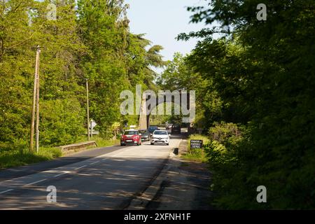 Langeac, France - May 27, 2023: A sunny road winds through a verdant landscape, leading to a stone archway in Langeac, France. Stock Photo