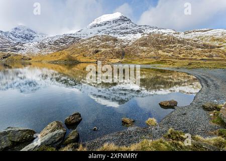 Crib Goch (Red ridge) part of the Snowdon horseshoe, covered in snow reflected in Llyn Llydaw, with the summit of Mount Snowdon. Snowdonia National Park, North Wales, UK, March 2017. Stock Photo