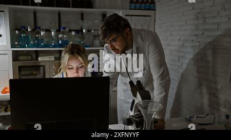 Two scientists, a man and a woman, intently analyze data on a computer screen in a well-equipped laboratory. Stock Photo